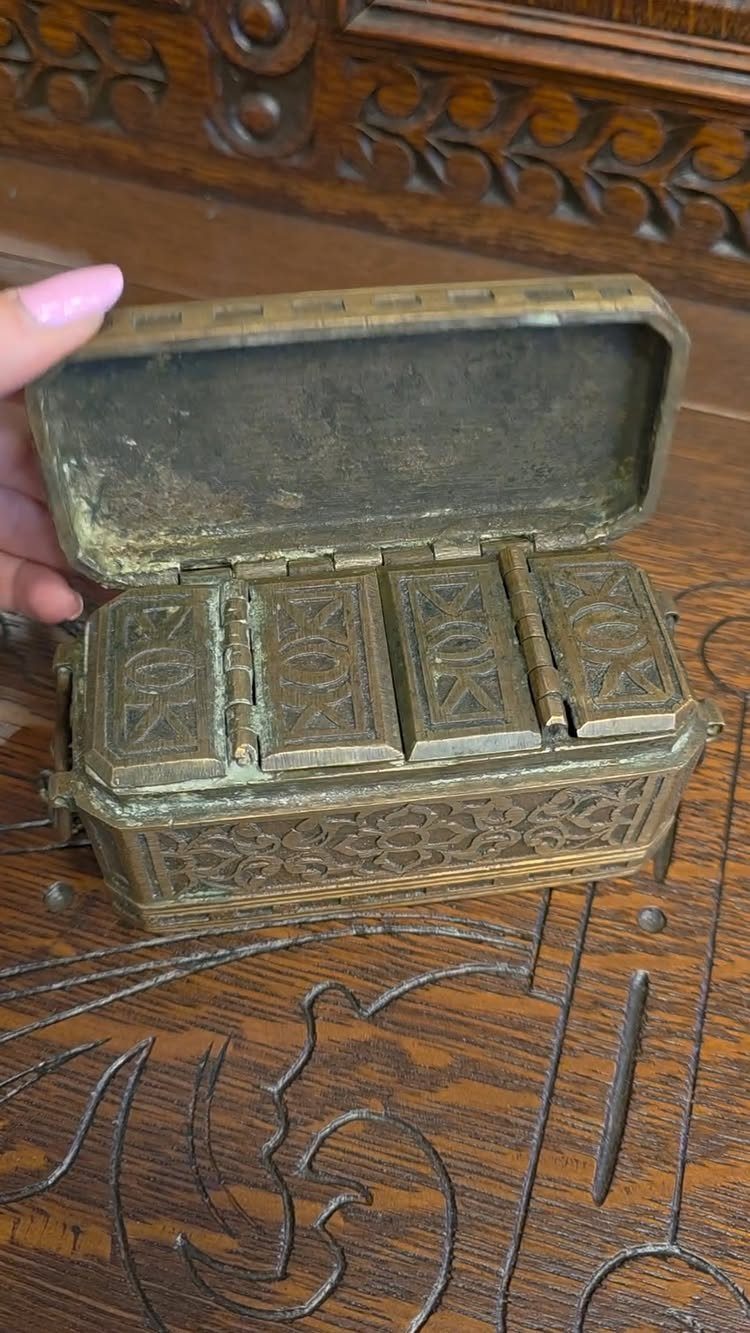 Vintage brass ring box with ornate engravings open on a carved wooden table