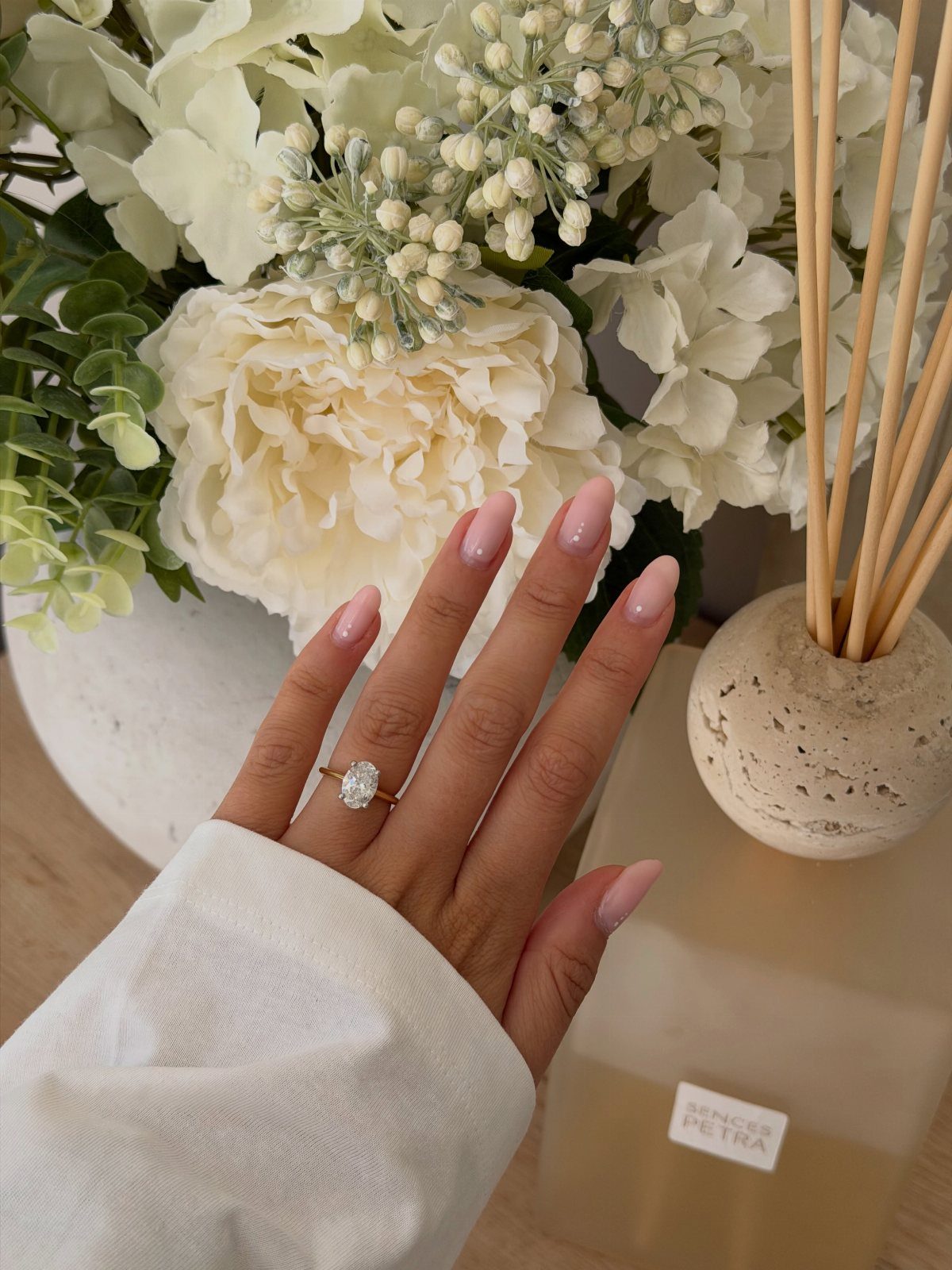 Hand wearing a diamond engagement ring posed in front of white floral bouquet