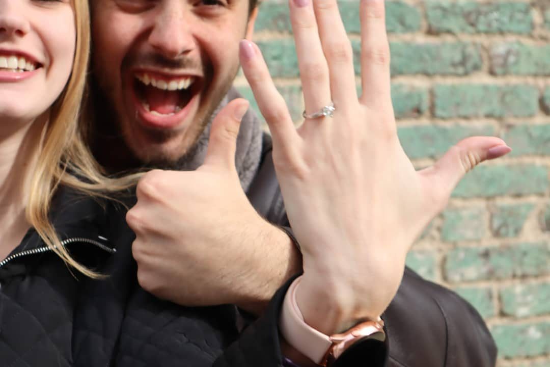 Couple posing with a diamond engagement ring displayed on a woman's hand.
