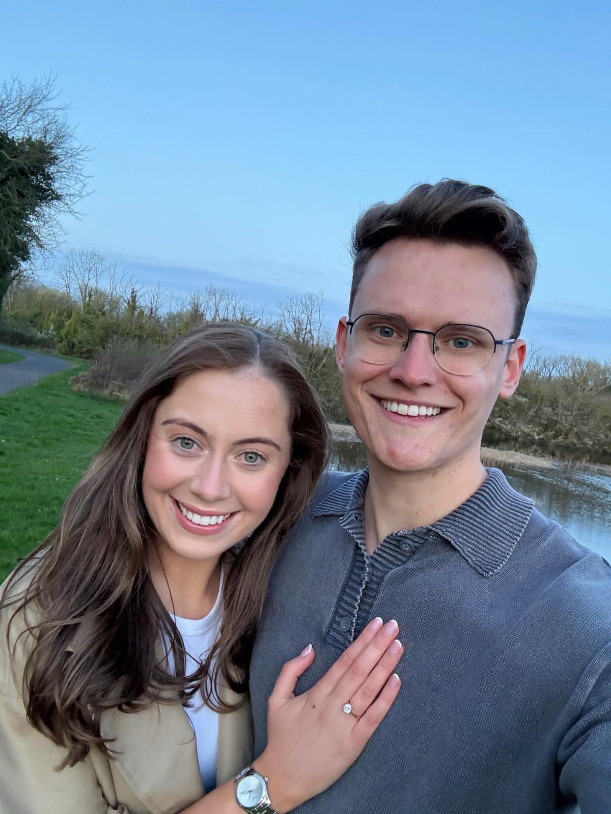 Smiling couple posing outdoors with a diamond engagement ring visible on her finger