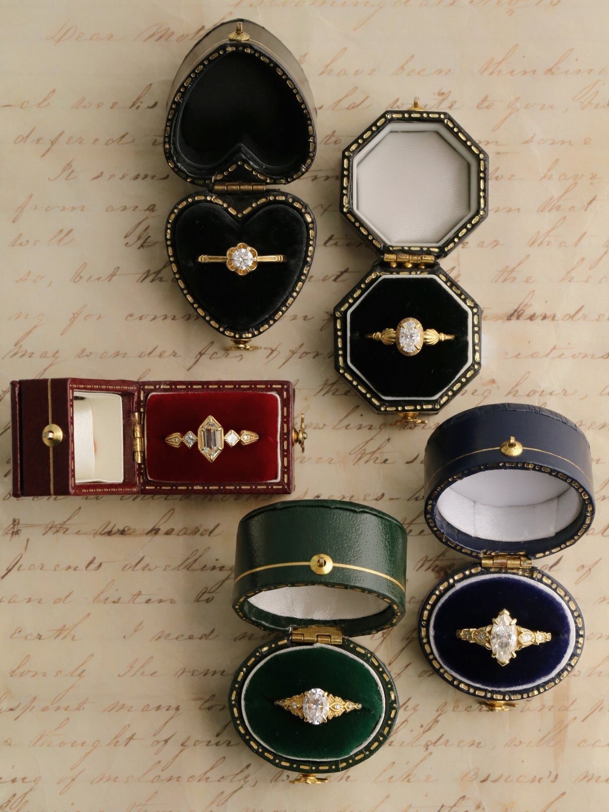Five gold diamond engagement rings in vintage velvet boxes on handwritten parchment paper