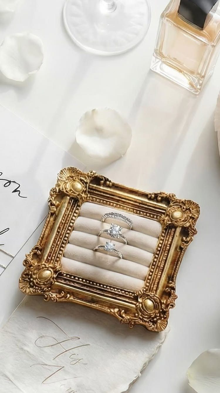 Three diamond rings in an ornate gold frame surrounded by white flower petals