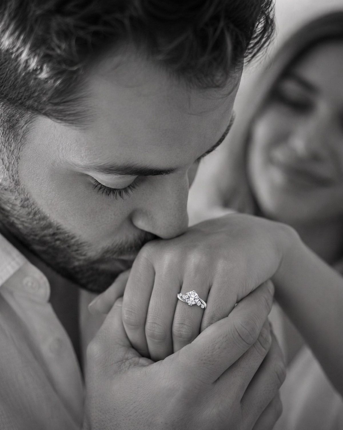 Man kissing a woman's hand featuring a diamond engagement ring in black and white