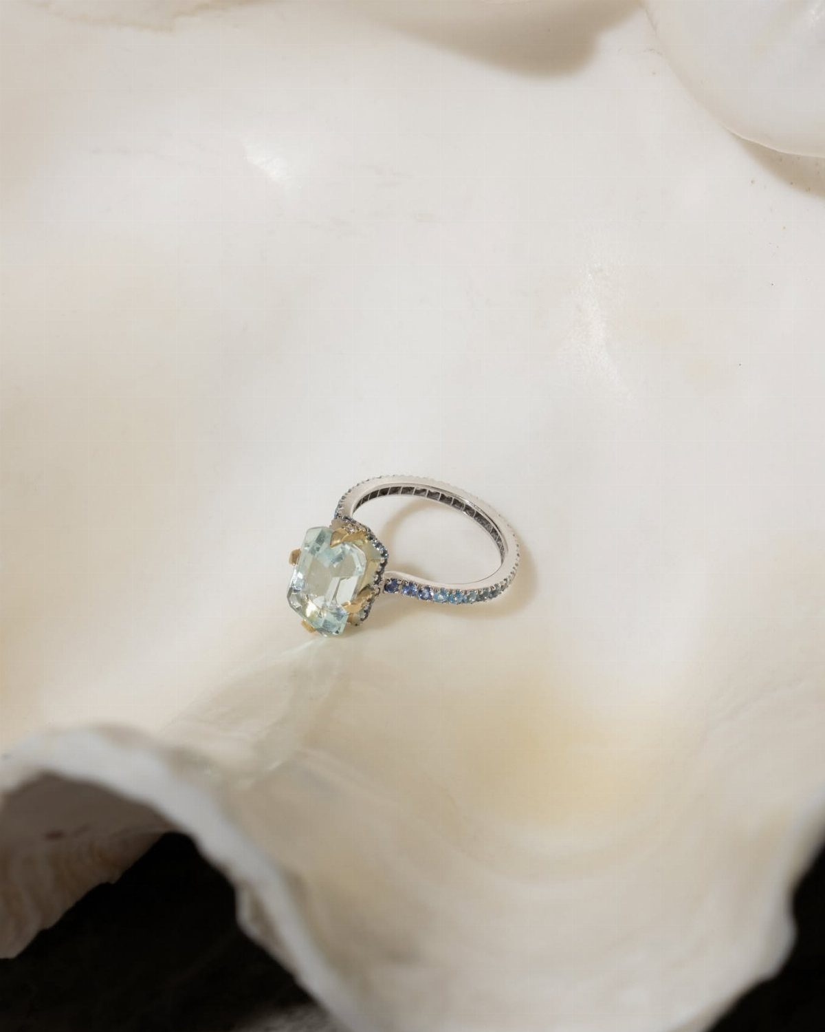 Silver engagement ring with blue gemstone resting inside a white textured seashell