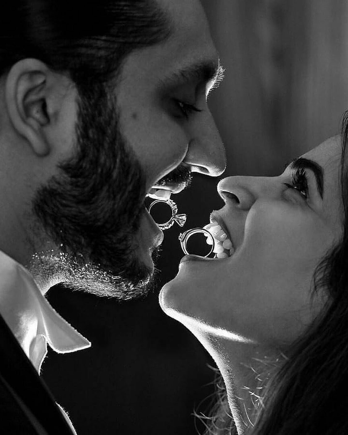 Couple holding engagement rings between their teeth in a black and white portrait