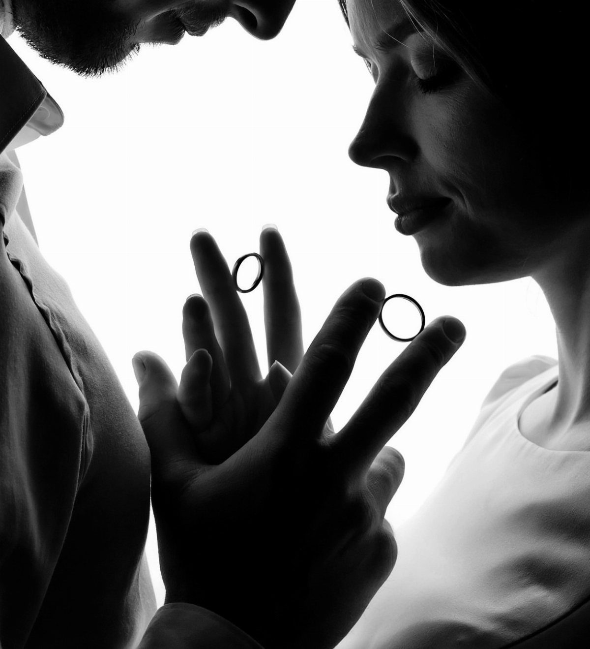Silhouette of a couple facing each other with rings visible on their fingers.