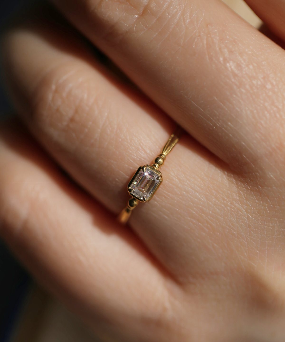 Gold ring with emerald-cut diamond on a person's finger in sunlight