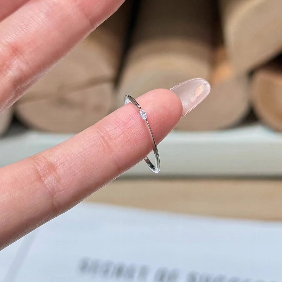 Thin silver ring with a single small diamond held by a finger.