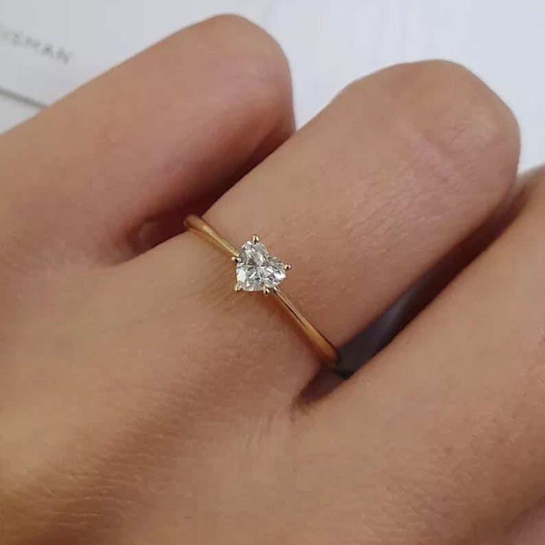 Gold ring with a single heart-shaped diamond worn on a person's finger.
