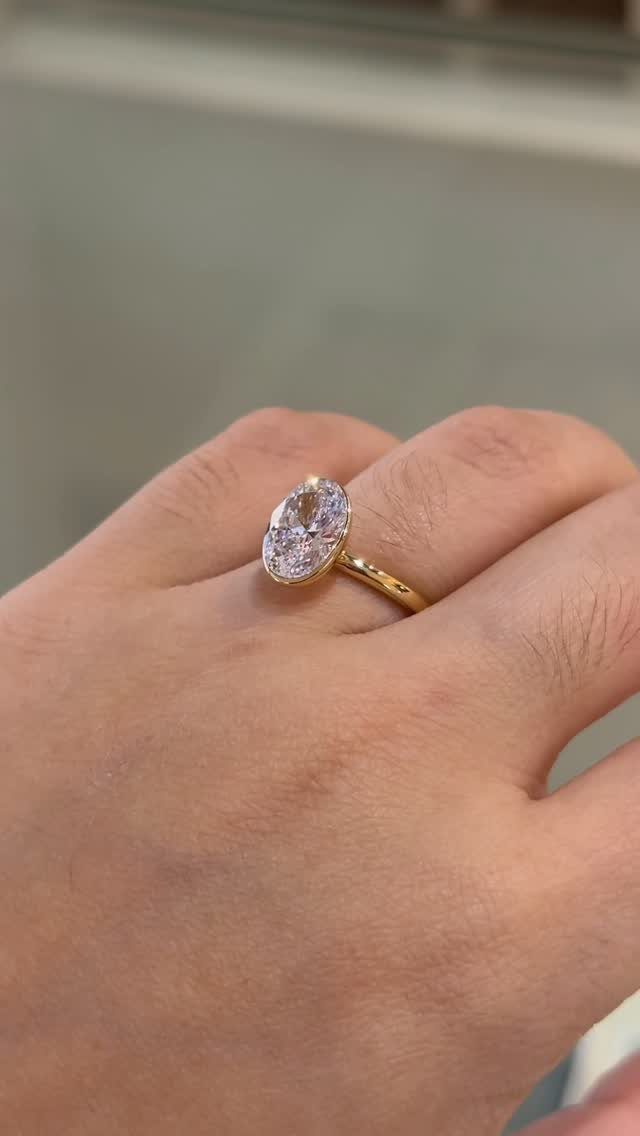 Gold engagement ring with a single oval clear stone on a finger