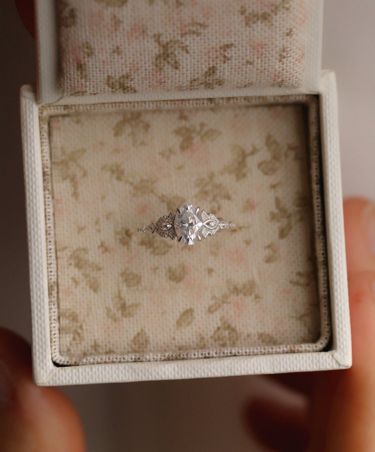 Silver single stone engagement ring resting in a floral fabric jewelry box.