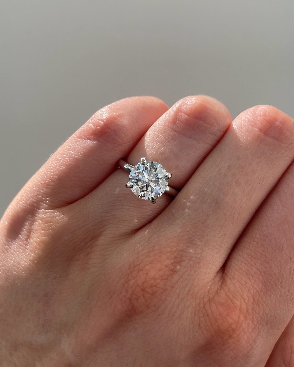 Round cut diamond engagement ring on a person's finger against a light background