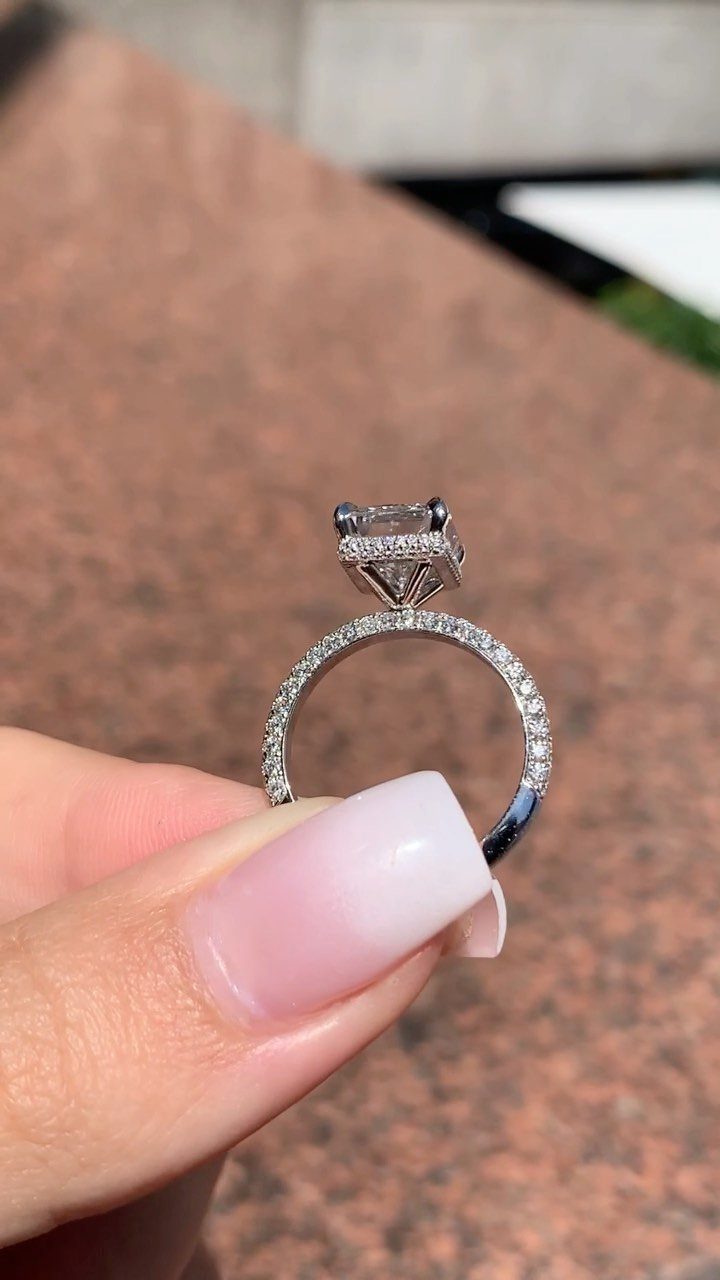 Silver engagement ring with square center diamond held by a manicured finger.