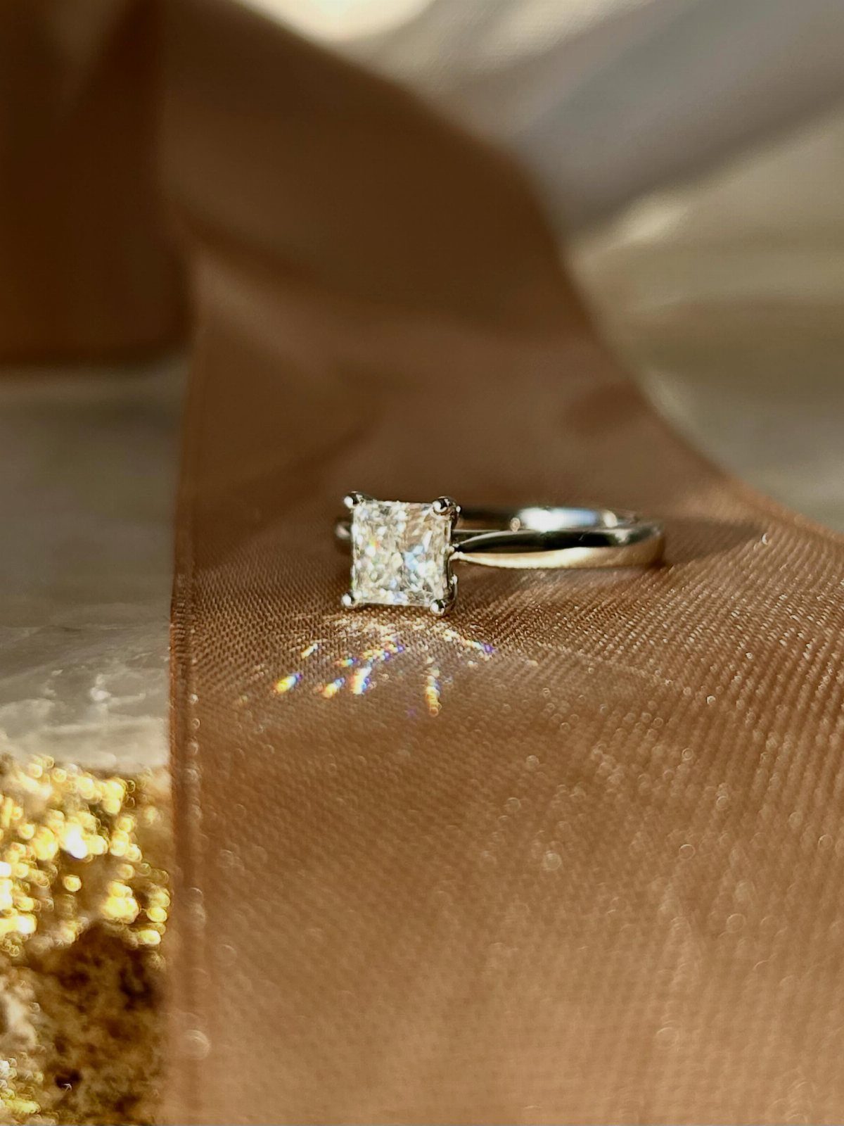 Silver engagement ring with a single square diamond on bronze fabric