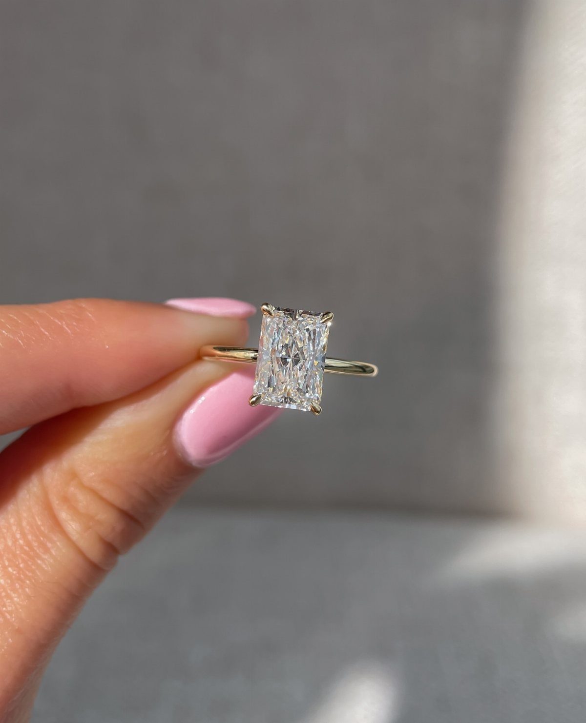 Gold engagement ring with a single rectangular diamond held by pink nails.