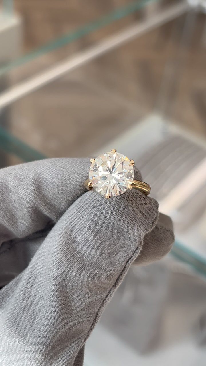 Gold engagement ring with a single round diamond held by a gloved hand.