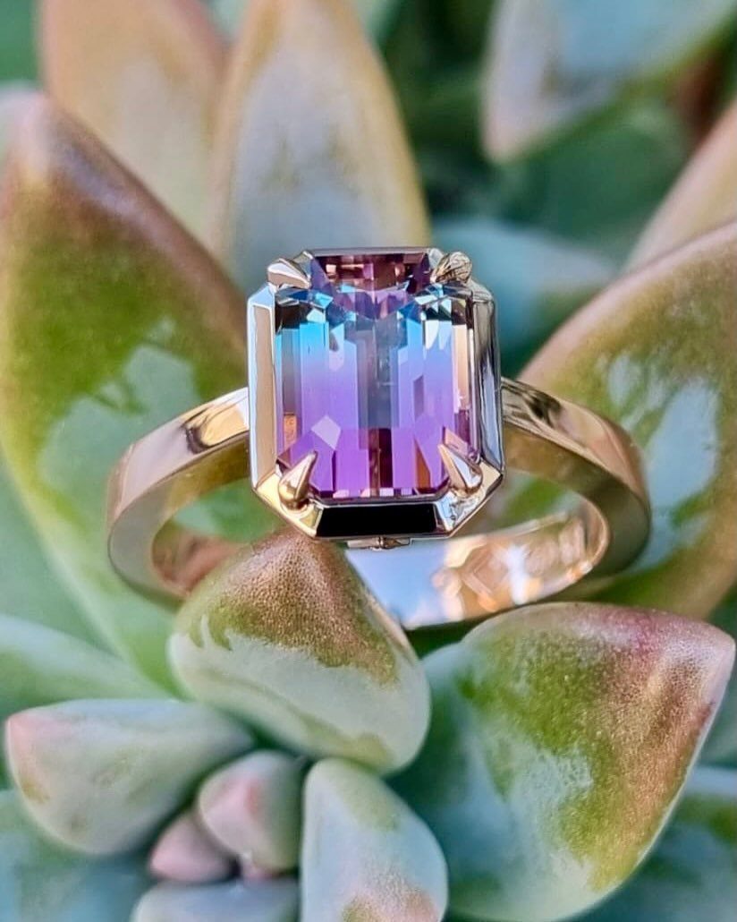 Gold ring with a purple emerald-cut gemstone resting on a succulent plant