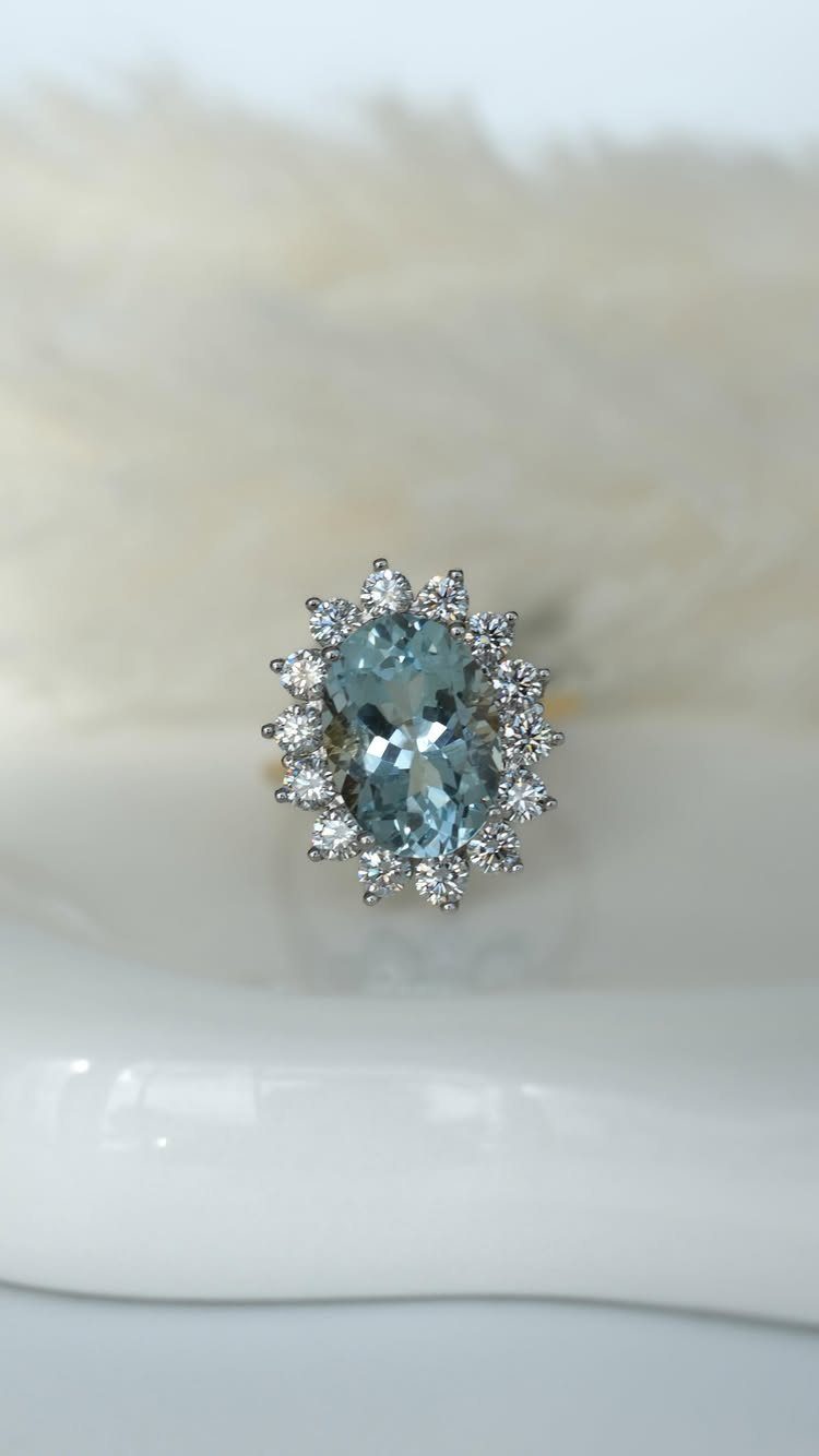 Oval light-blue gemstone ring surrounded by a halo of small clear diamonds.
