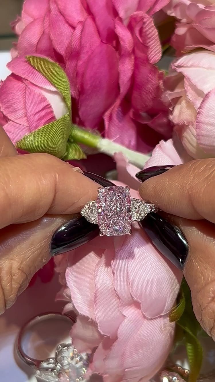 Silver ring with pink gemstone cluster held against pink flowers by manicured fingers