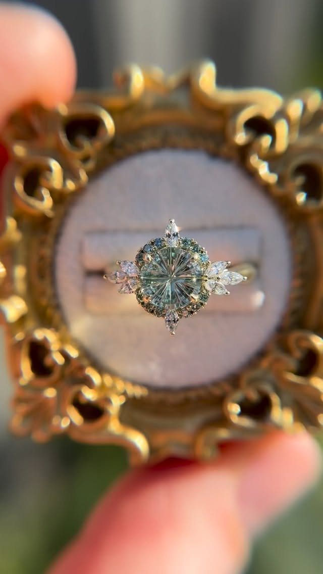 Gold engagement ring with a light green center stone and diamond accents.