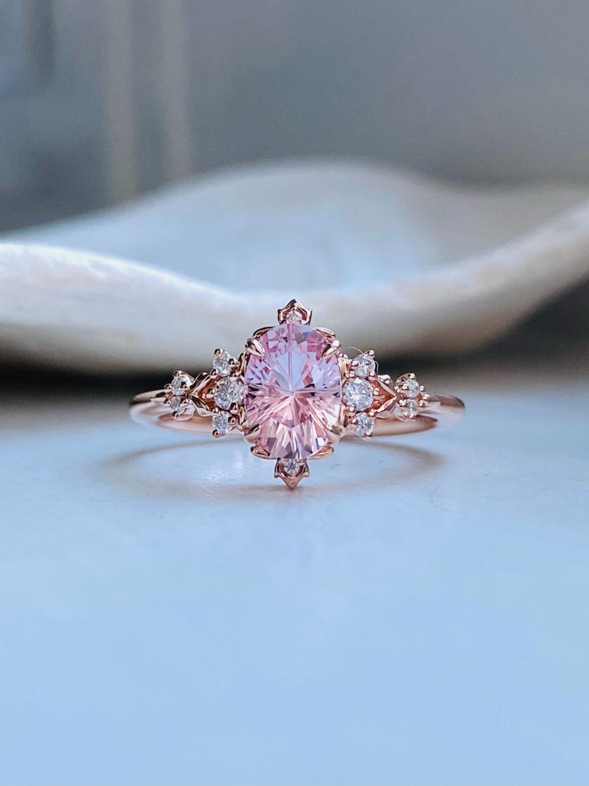 Rose gold engagement ring with a central oval pink sapphire and diamond accents.