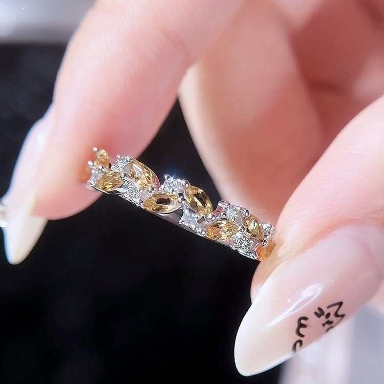 Silver ring with marquise-cut yellow gemstones and small diamonds held by fingers