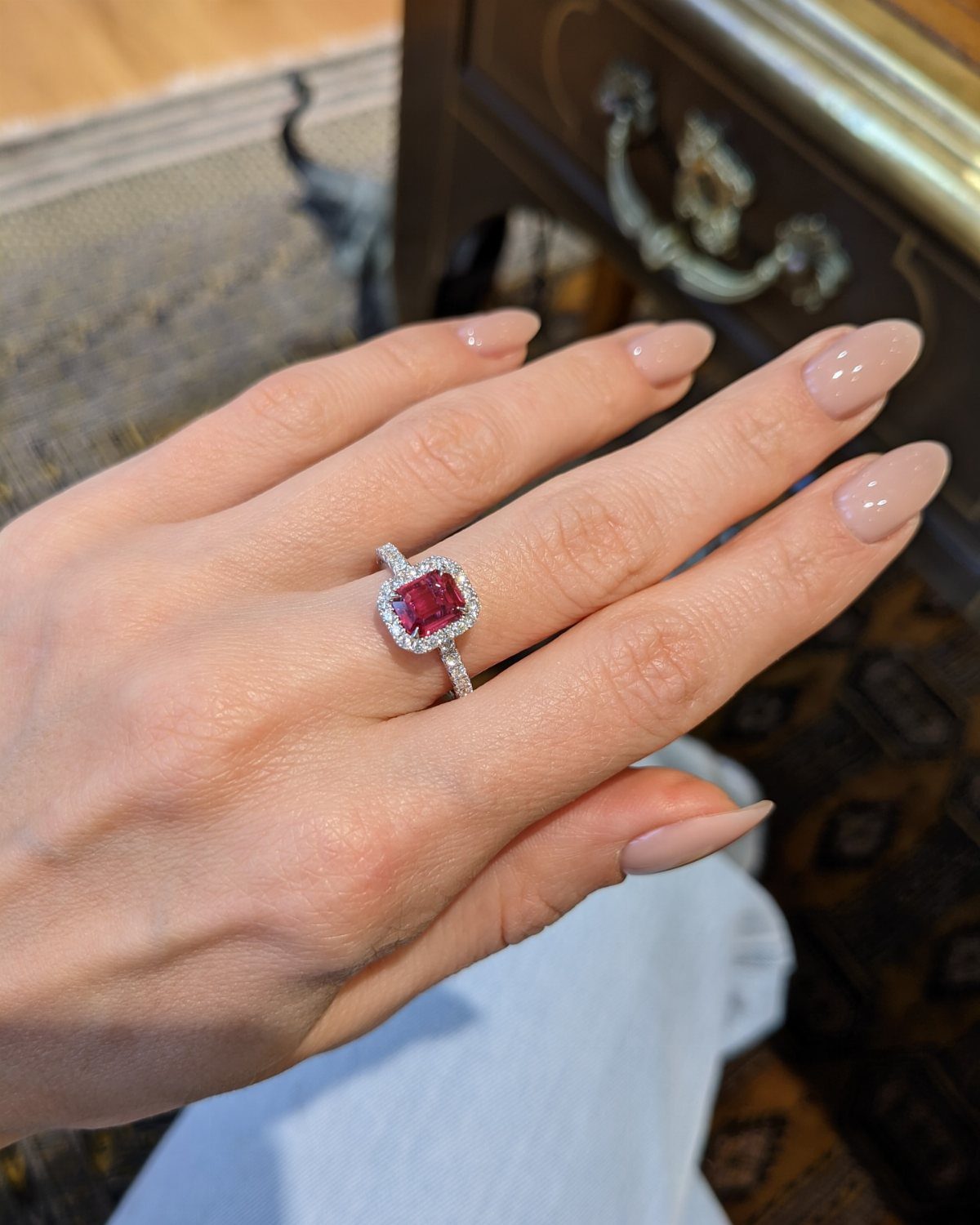 Silver ring with a square red ruby and diamond halo on a finger