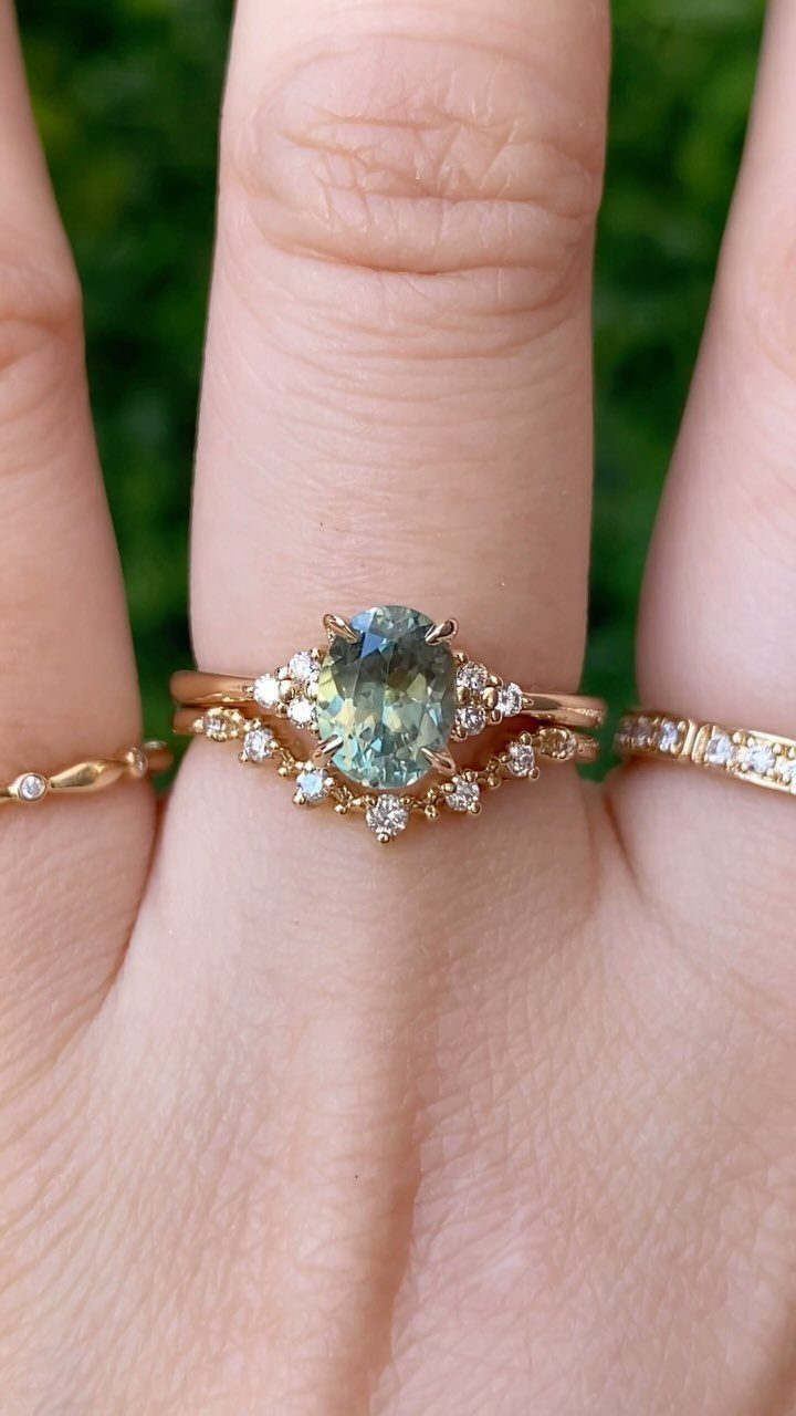 Gold engagement ring with an oval greenish-blue gemstone and small diamonds on a finger