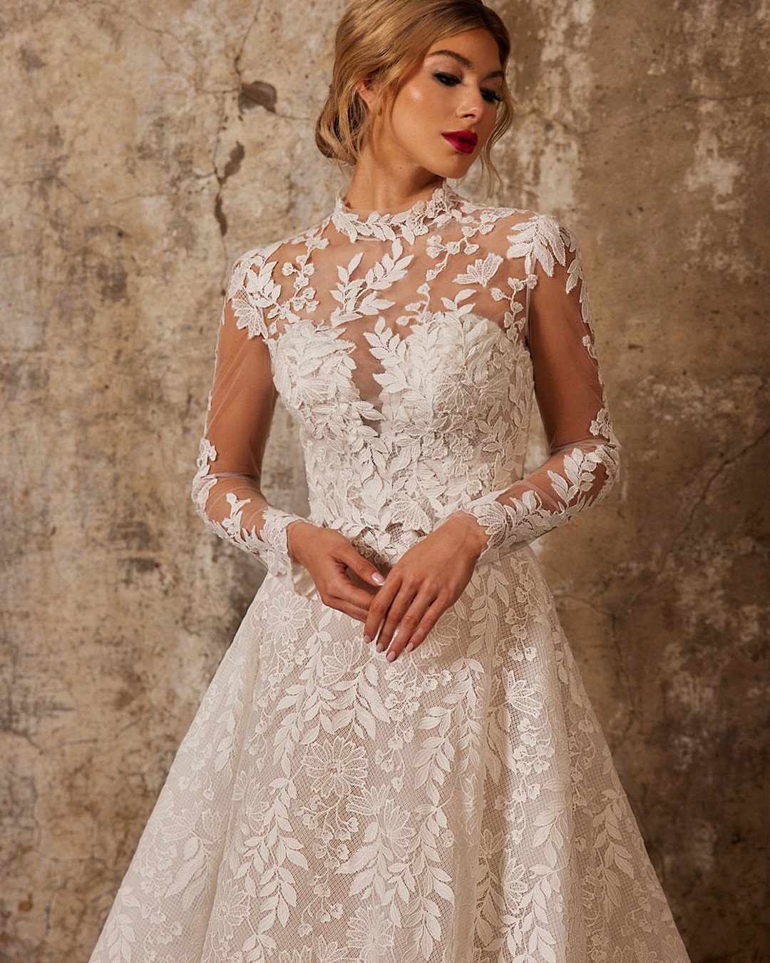 Woman in a white wedding dress with intricate floral lace overlay and sheer sleeves.
