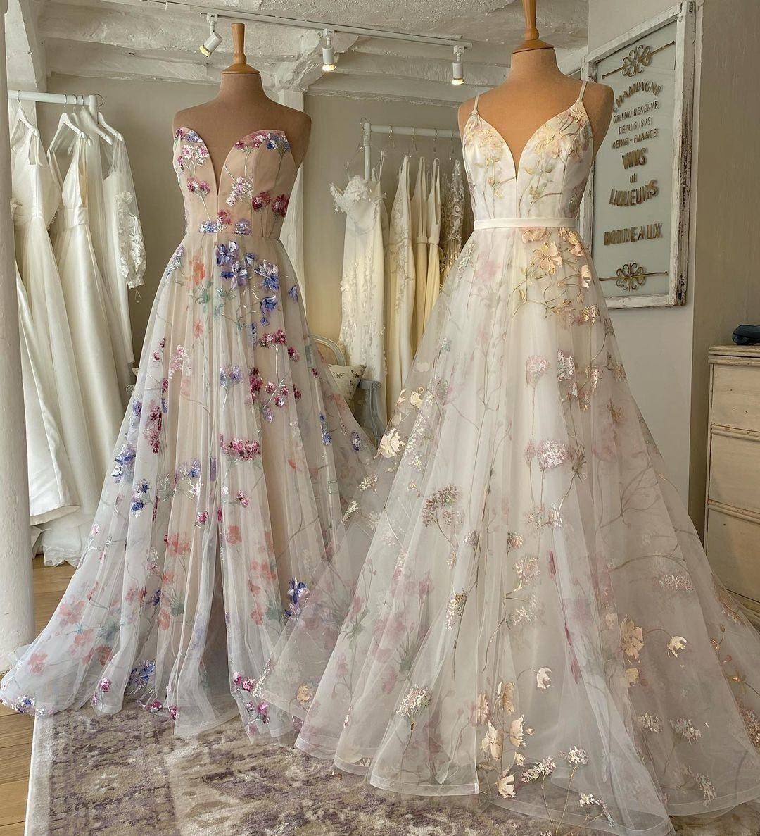Two white ball gown wedding dresses with colorful floral embroidery on mannequins.