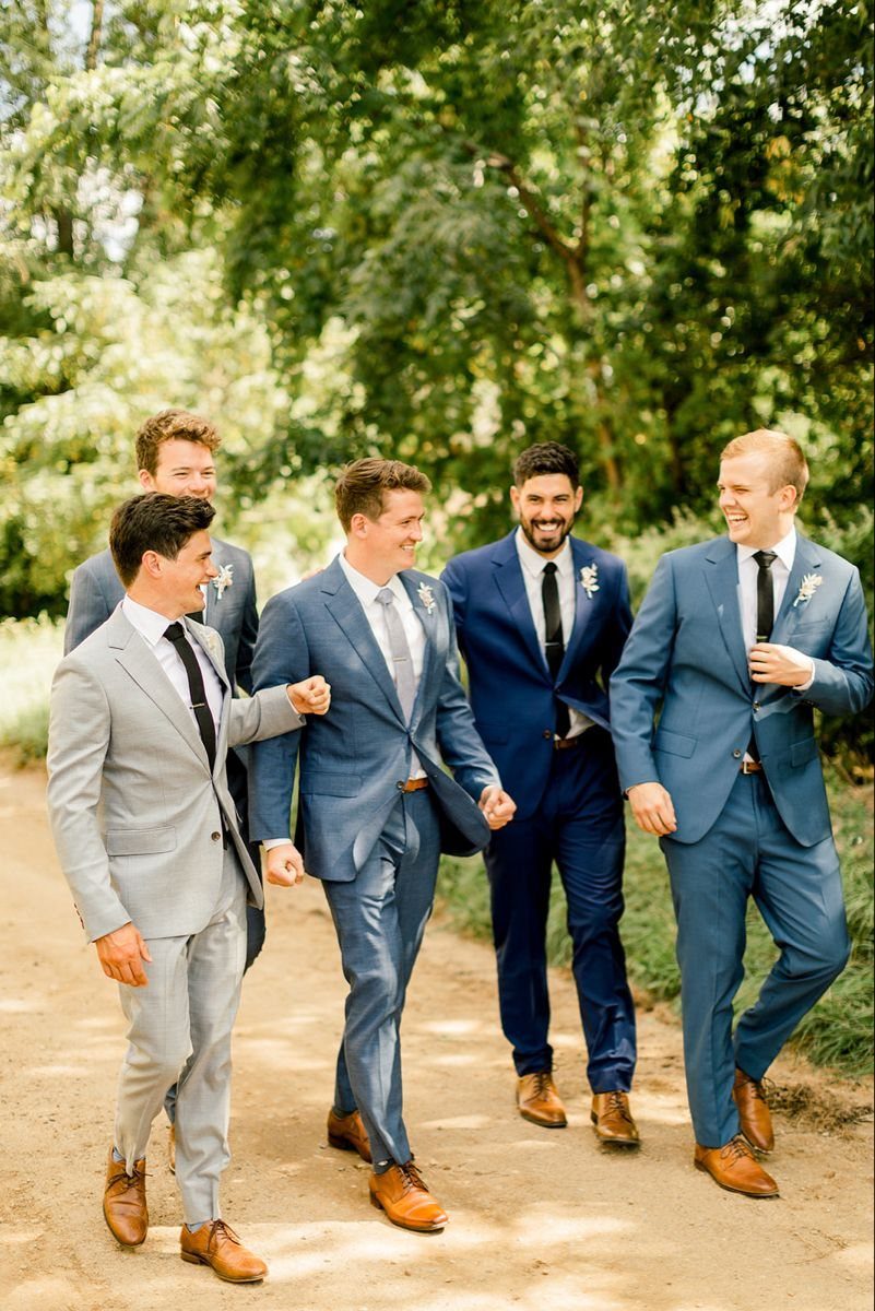 Five groomsmen in coordinating blue and grey suits walking together on a path.