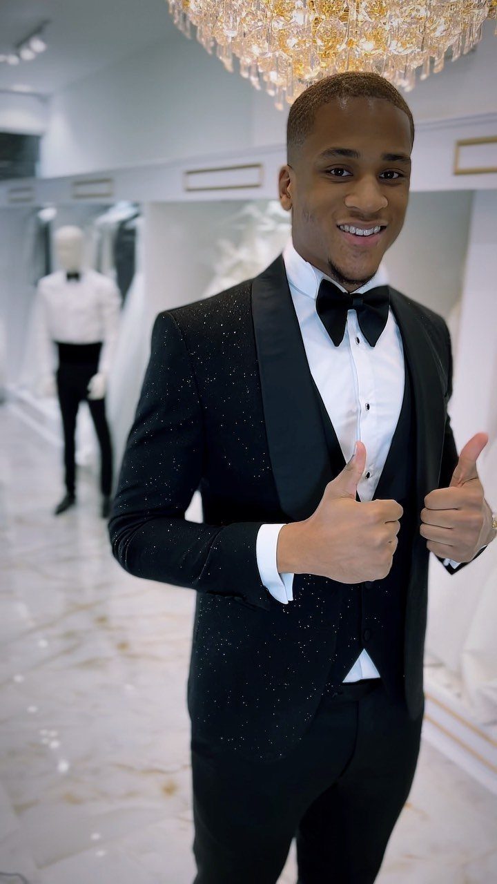 Man in a shimmering black tuxedo and bow tie giving two thumbs up.