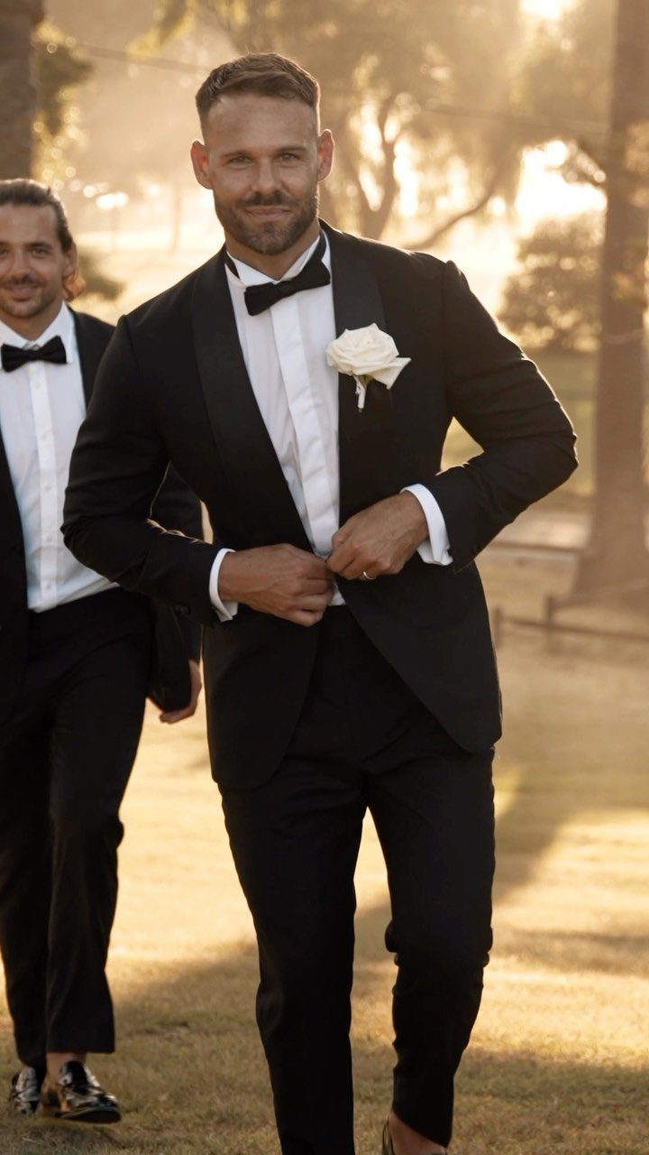 Men in black formal tuxedos with bow ties and white rose boutonniere outdoors.