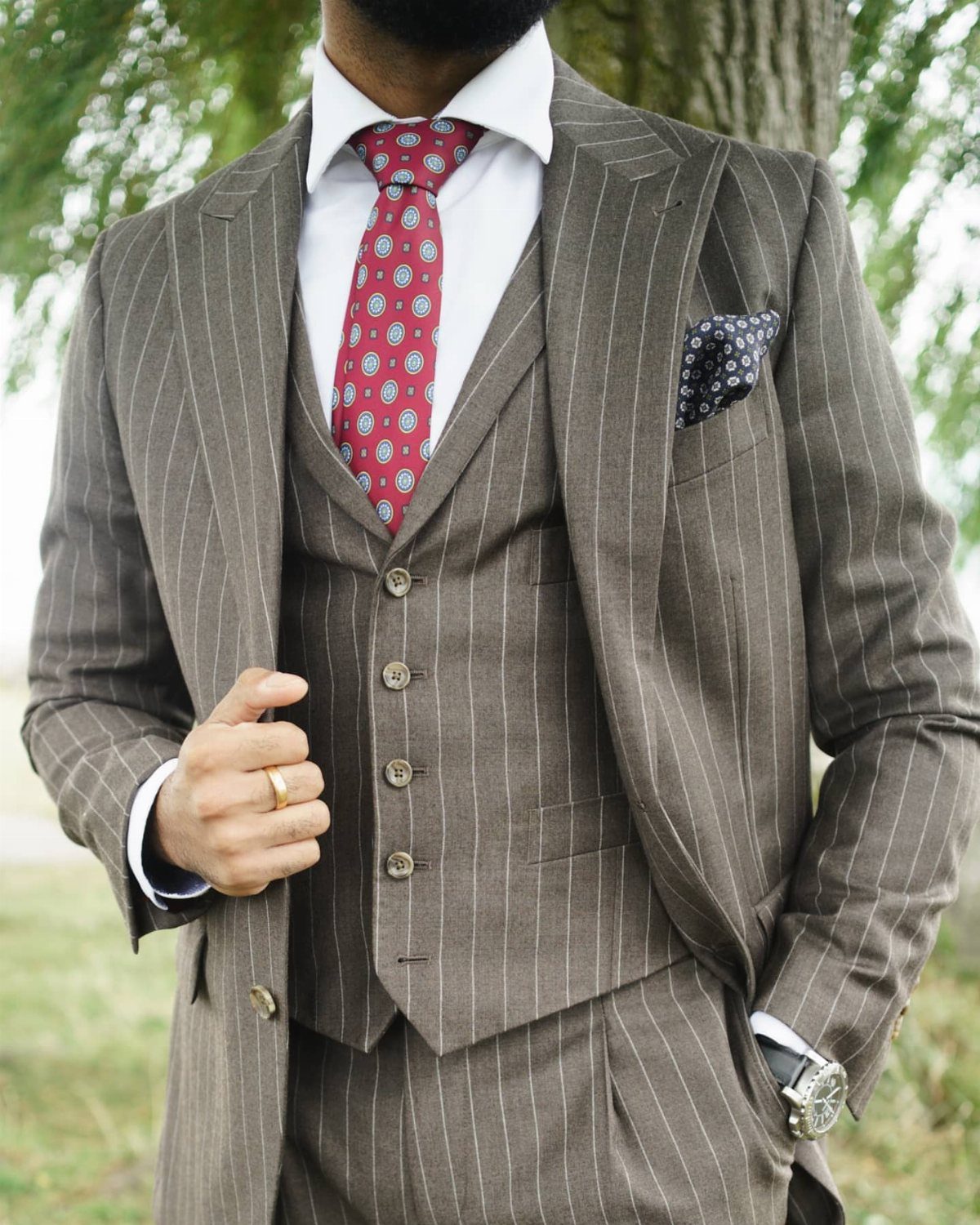 Man in brown pinstripe suit with red patterned tie and pocket square.