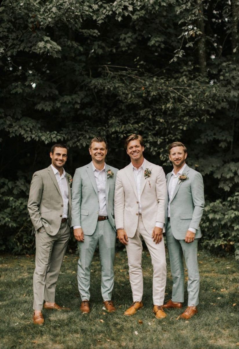 Four men in light-colored coordinating suits standing together in a grassy outdoor setting.