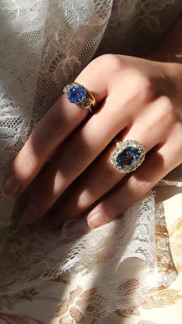 Hand wearing two gold rings with blue gemstones on white lace fabric