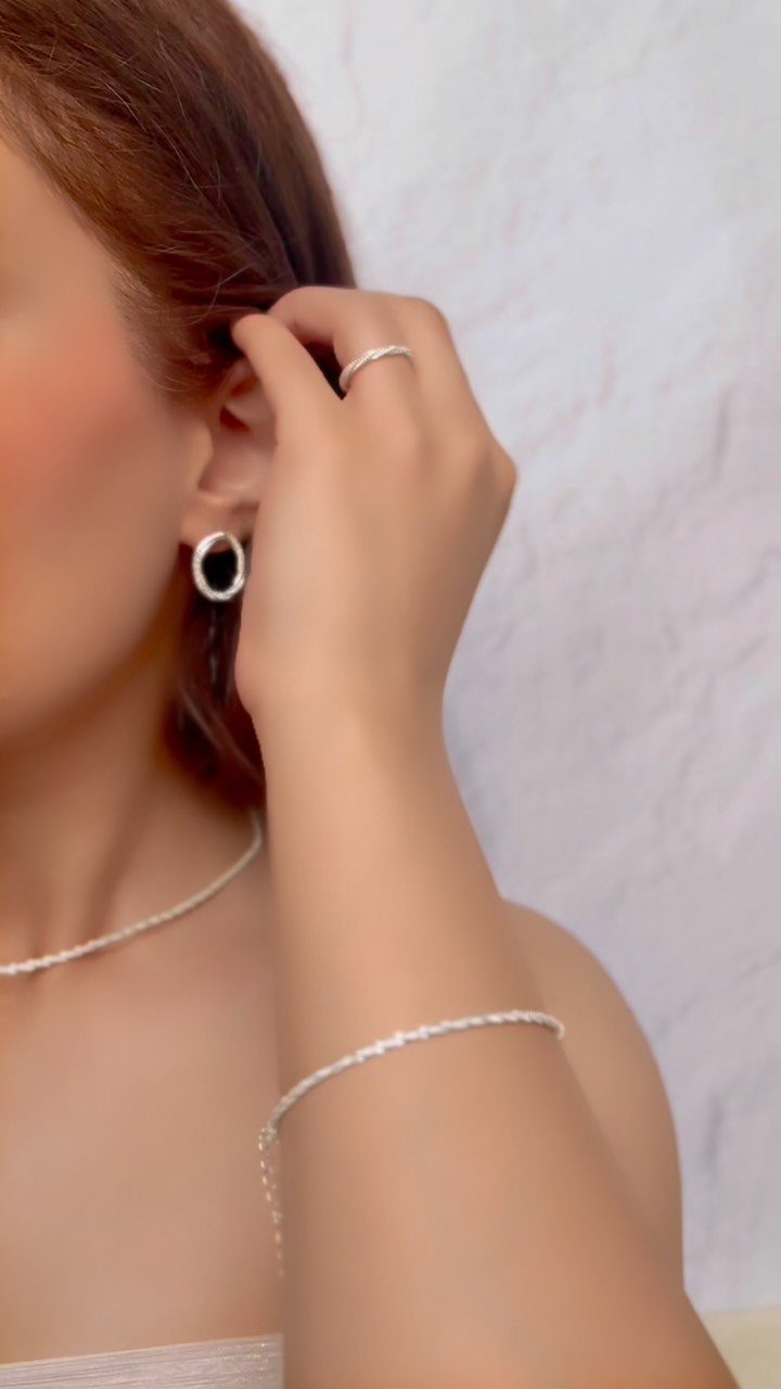 Woman wearing delicate silver jewelry including a thin necklace, hoop earring, and bracelet.