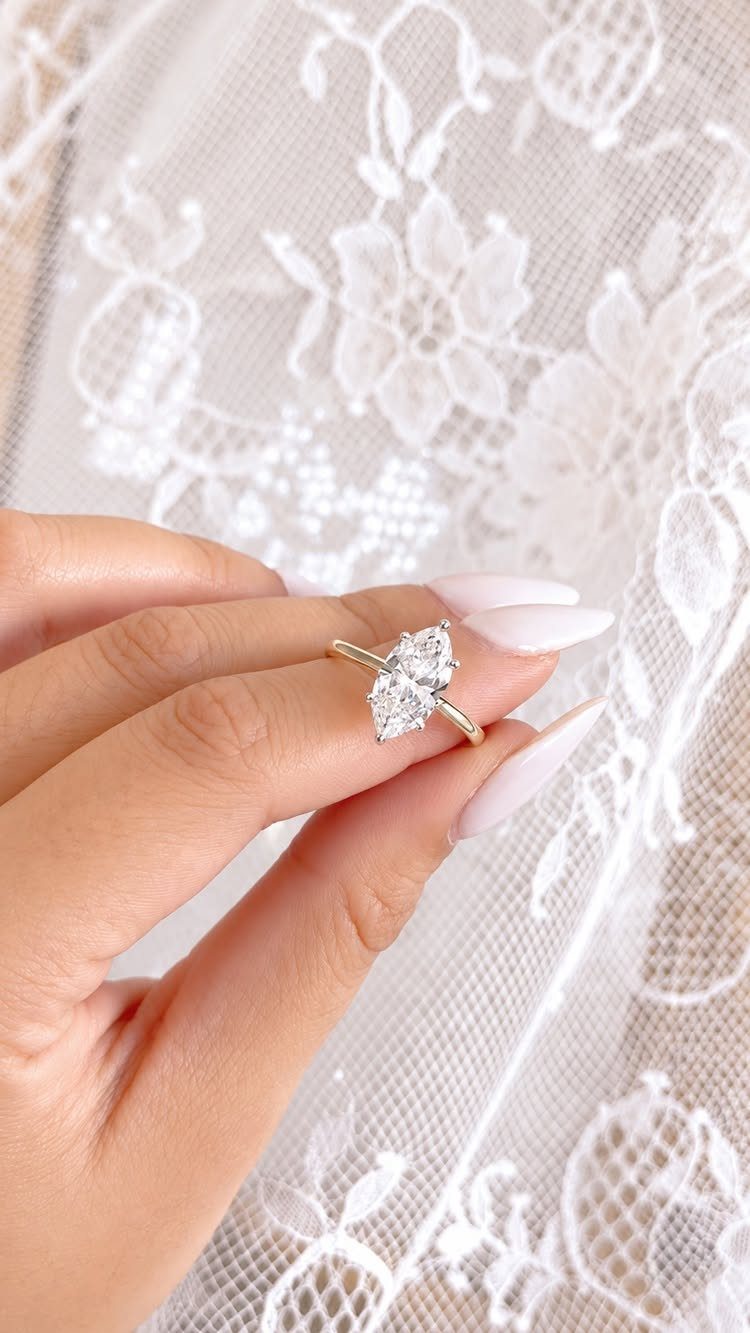 Gold pear-shaped diamond ring on a finger against white lace fabric