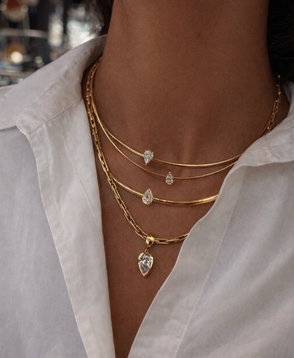 Layered gold necklaces with teardrop gemstones worn with a white collared shirt