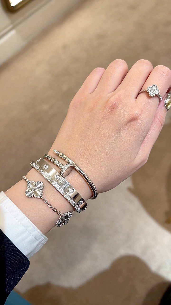 Hand and wrist wearing diamond rings and silver bracelets with a white sleeve.