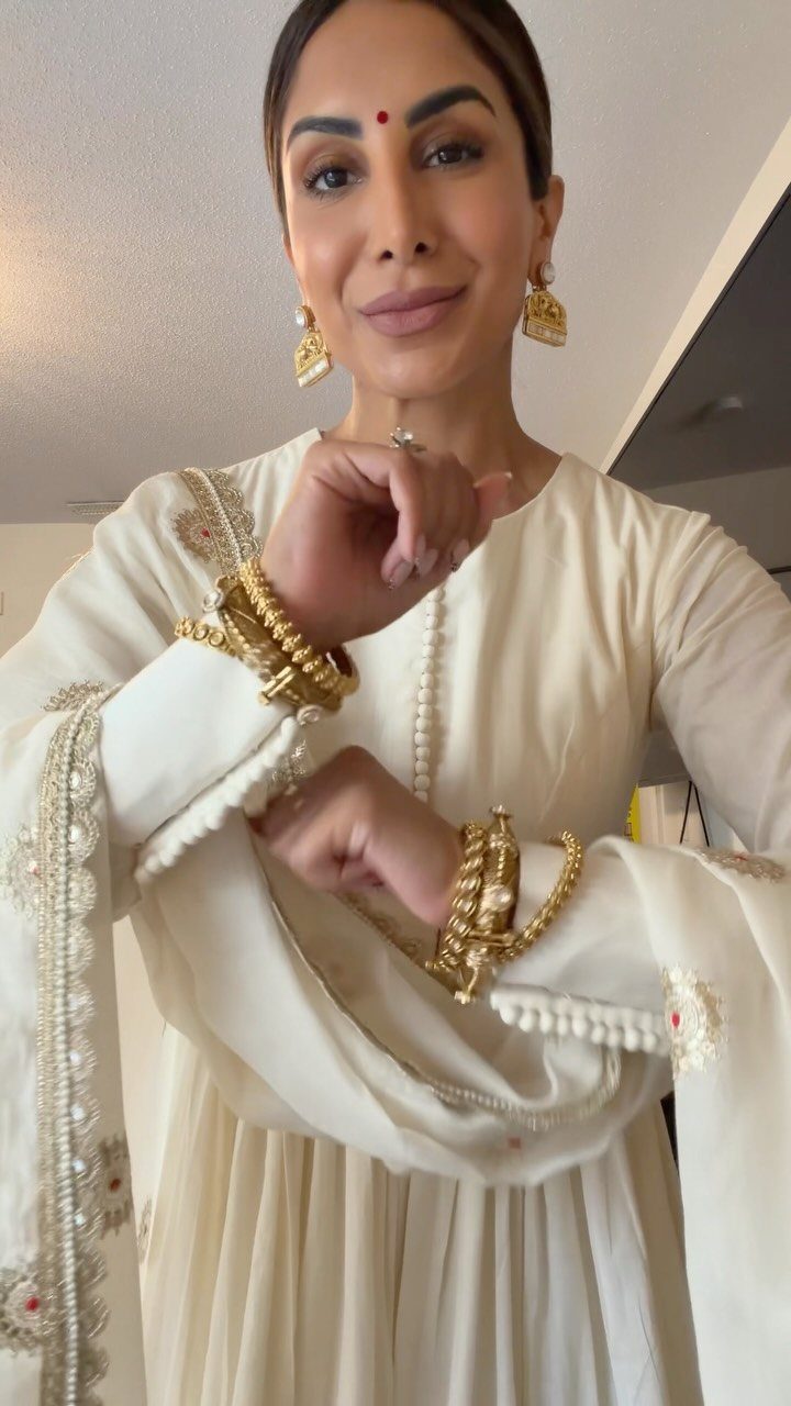 Woman in white traditional Indian dress wearing gold earrings and gold bangles.