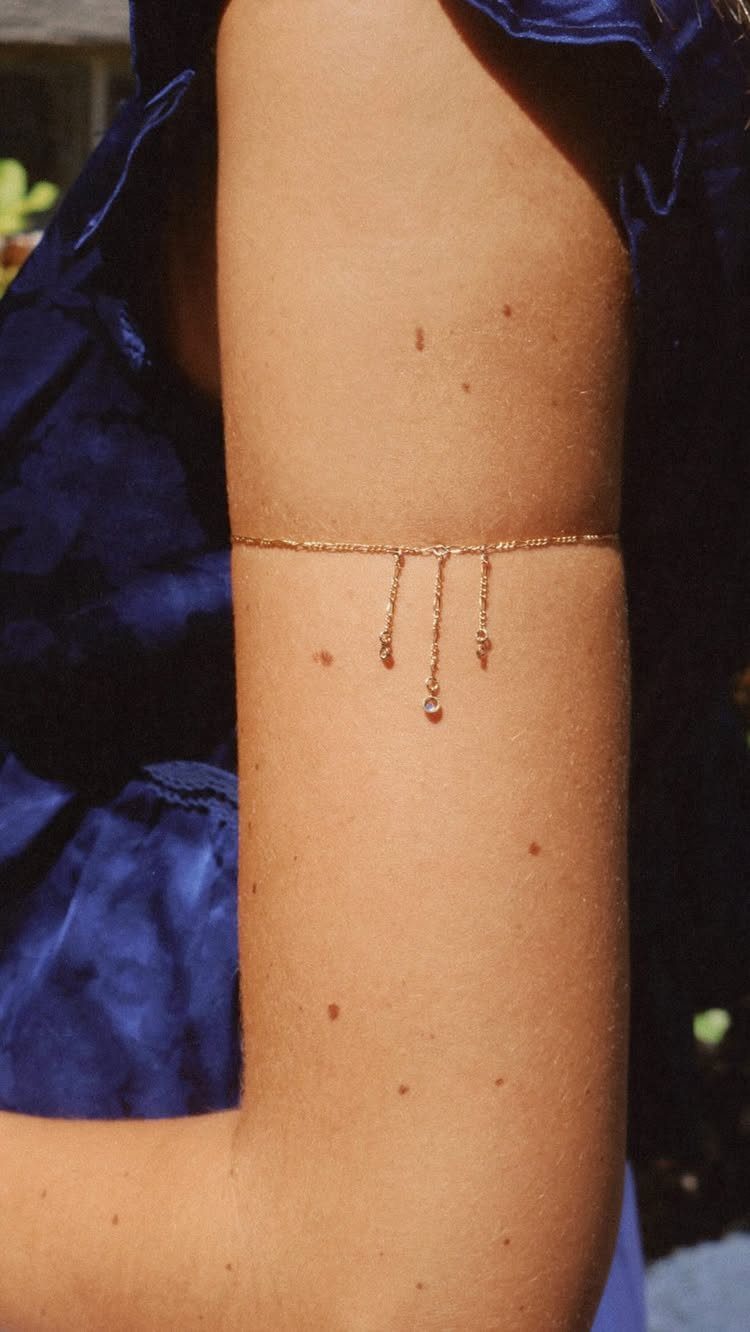 Gold chain arm cuff with dangling pendants worn on a bare upper arm