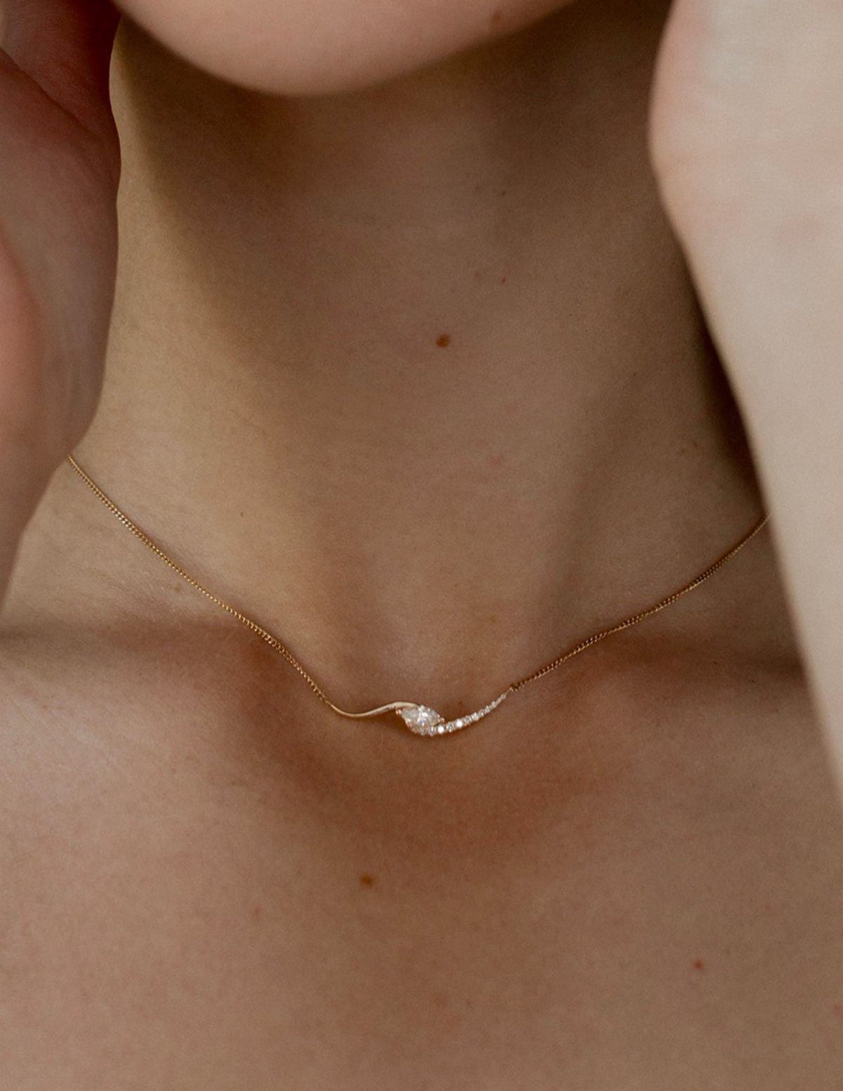 Delicate gold chain necklace with a small sparkling pendant on a person's neck.