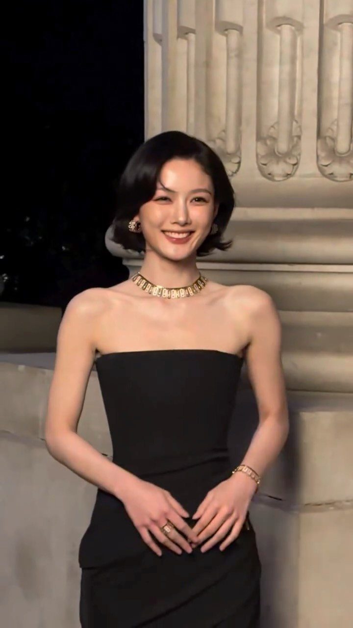 Woman in black strapless dress wearing a gold necklace, earrings, and bracelet.