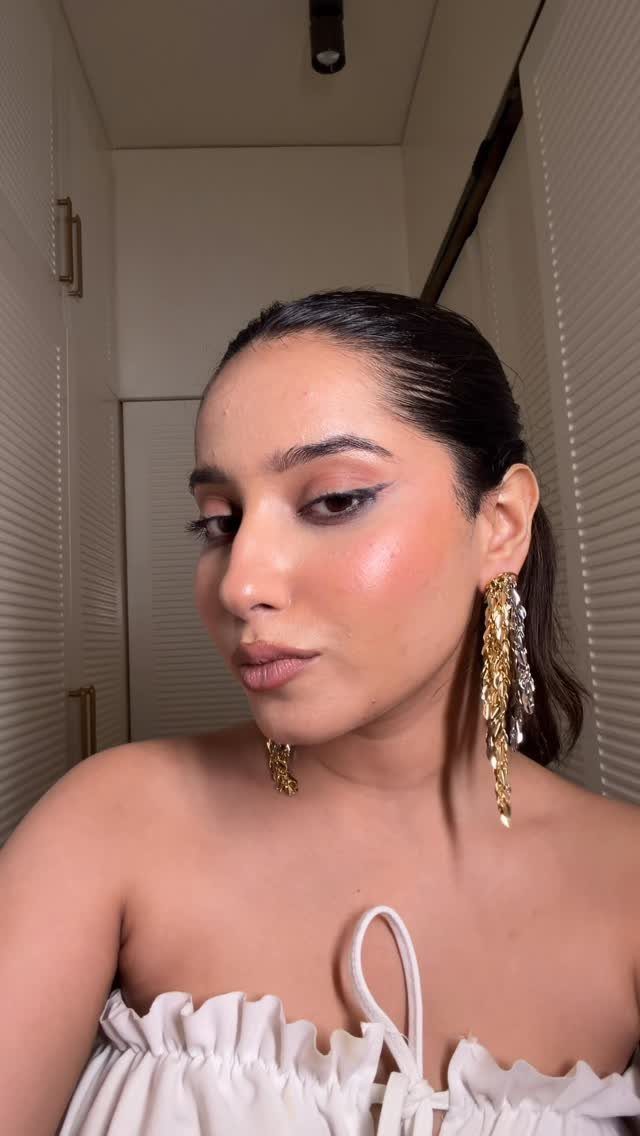 Woman wearing long gold chain earrings and a white strapless ruffled top.