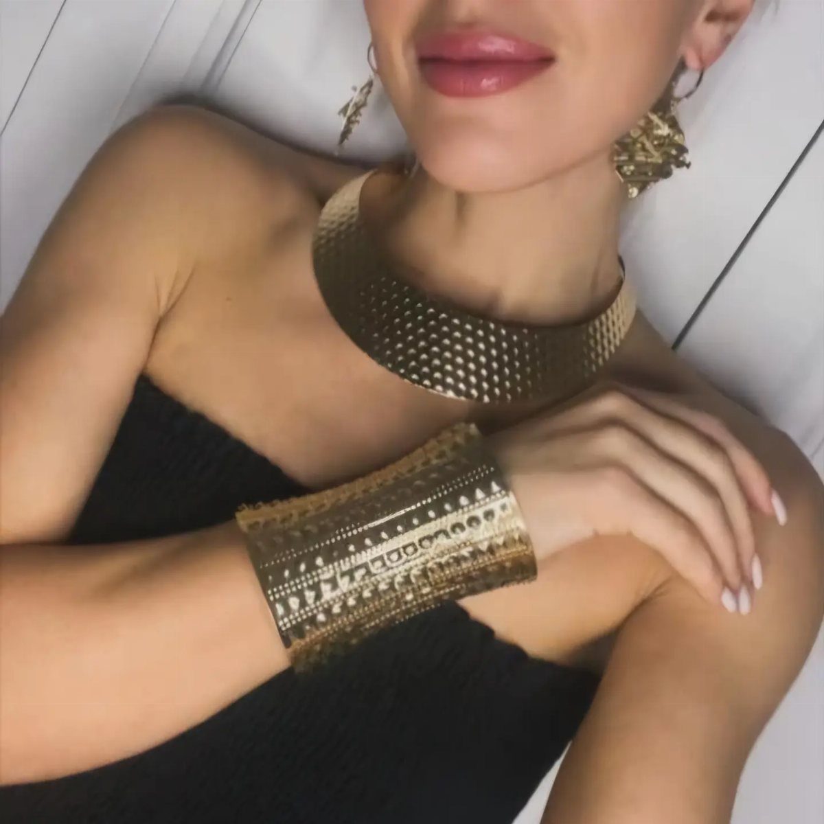 Woman in black strapless dress wearing a gold collar necklace and cuff bracelet