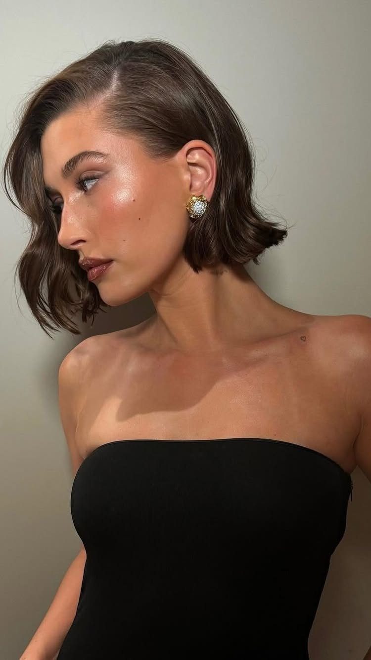 Woman in a black strapless dress wearing large gold and diamond stud earrings.