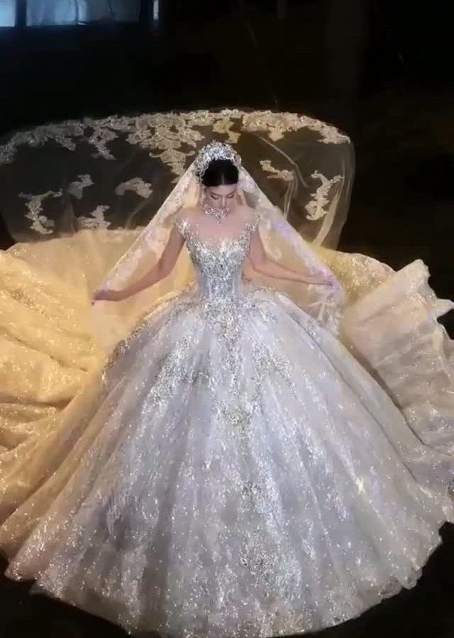 Woman in a voluminous sparkly white ballgown wedding dress with a long lace veil.