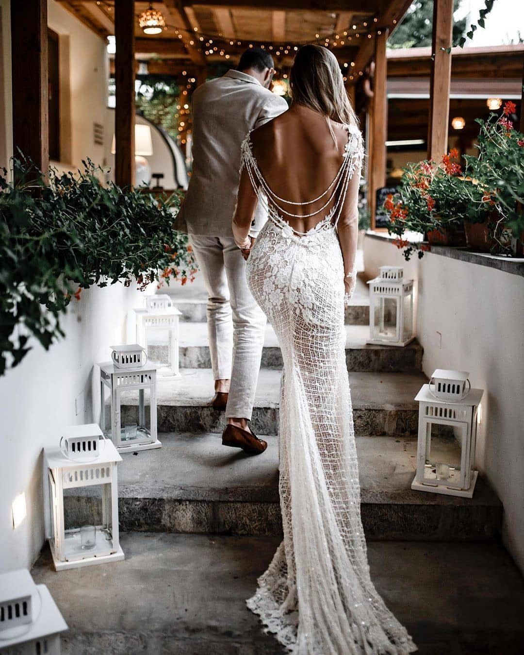 Woman in a backless lace wedding dress walking up stone steps with a groom
