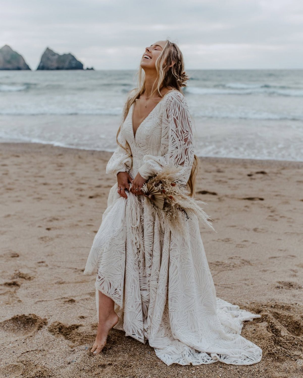 Woman in a bohemian white lace wedding dress standing on a sandy beach